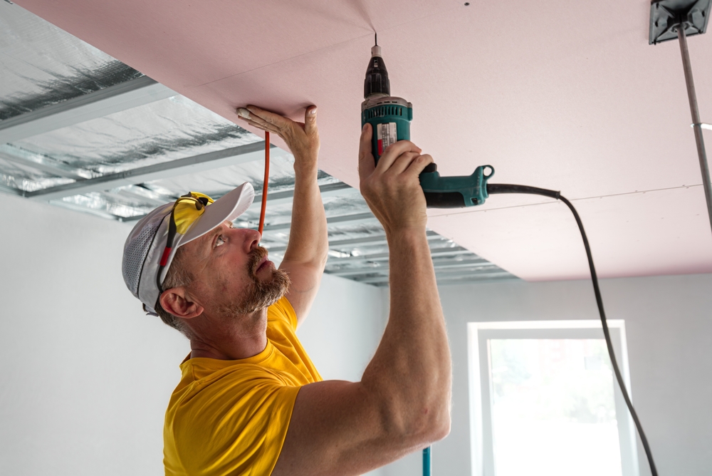 Especialista realizando la instalación de drywall en una estructura de techo metálica usando un taladro eléctrico