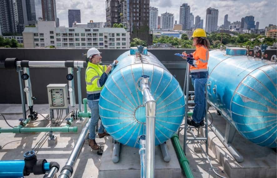 Dos operarios técnicos con equipo de seguridad realizando la revisión y mantenimiento para la impermeabilización de tanques de agua en una azotea urbana
