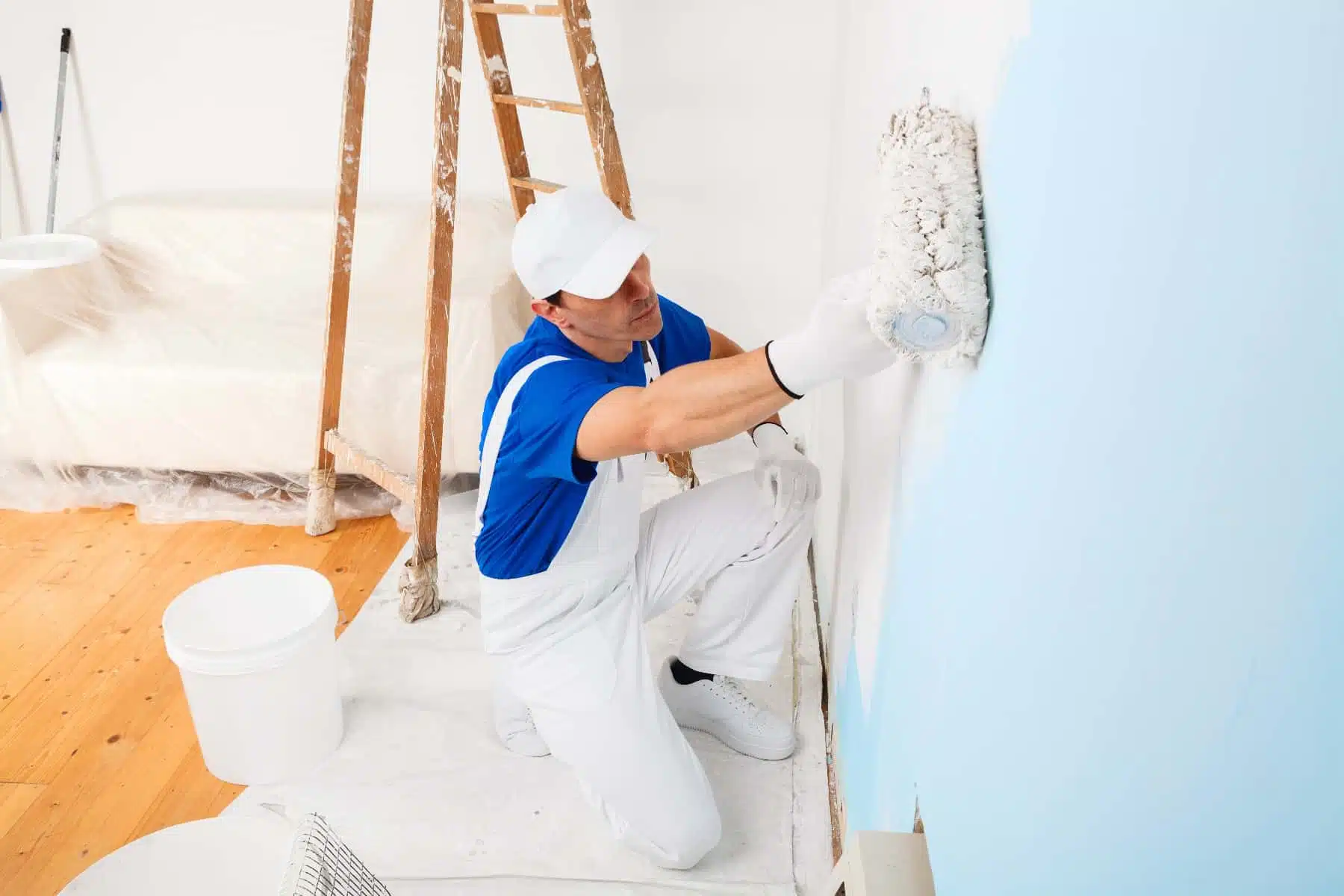 Pintor profesional con uniforme blanco y azul realizando un servicio de pintura interior en una pared con rodillo y pintura celeste