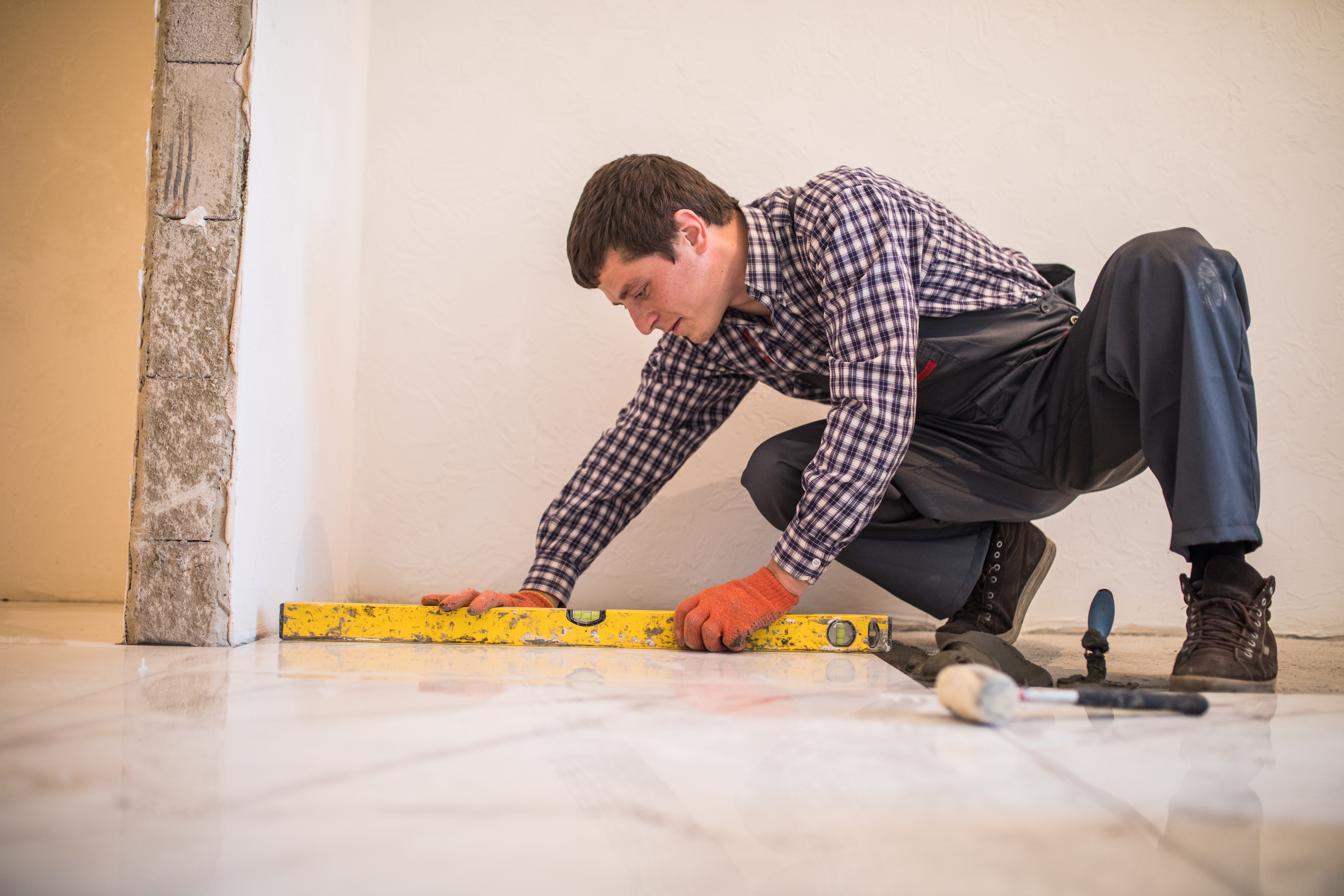 Profesional verificando la nivelación de grandes baldosas blancas en el piso con un nivel de burbuja, un paso clave tras calcular metros cuadrados para la compra de material
