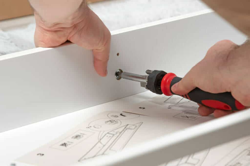 Primer plano de un profesional atornillando una tabla de mueble con un destornillador manual, como parte del servicio de armado de muebles 