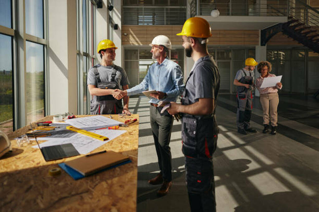 Ejecutivos y obreros con cascos revisando planos y cerrando un acuerdo para la planificación y ejecución del diseño de oficinas modernas en un edificio 