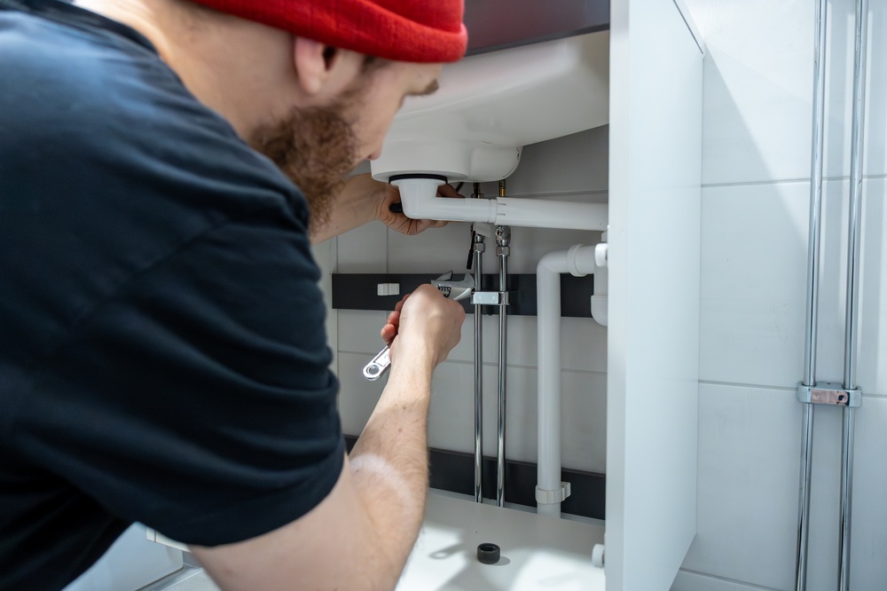  Plomero utilizando una llave ajustable en las tuberías inferiores de un mueble de baño para inspeccionar y destapar una cañería metálica 