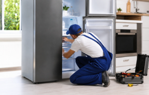 Técnico realizando reparación de neveras mientras revisa una fuga de agua en una cocina moderna
