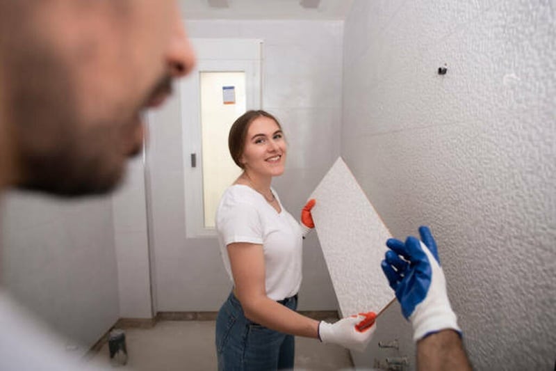 Decoración de baños en pareja con nuevos azulejos Pareja sonriente instalando nuevos azulejos blancos durante una reforma del hogar, disfrutando del proceso de decoración de baños con un toque moderno y funcional