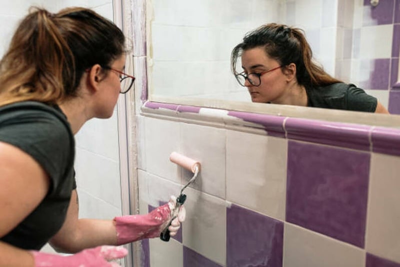 Decoración de baños con pintura en azulejos antiguos Mujer pintando azulejos de baño con rodillo pequeño en un proyecto de decoración de baños, renovando el espacio con estilo moderno y bajo costo