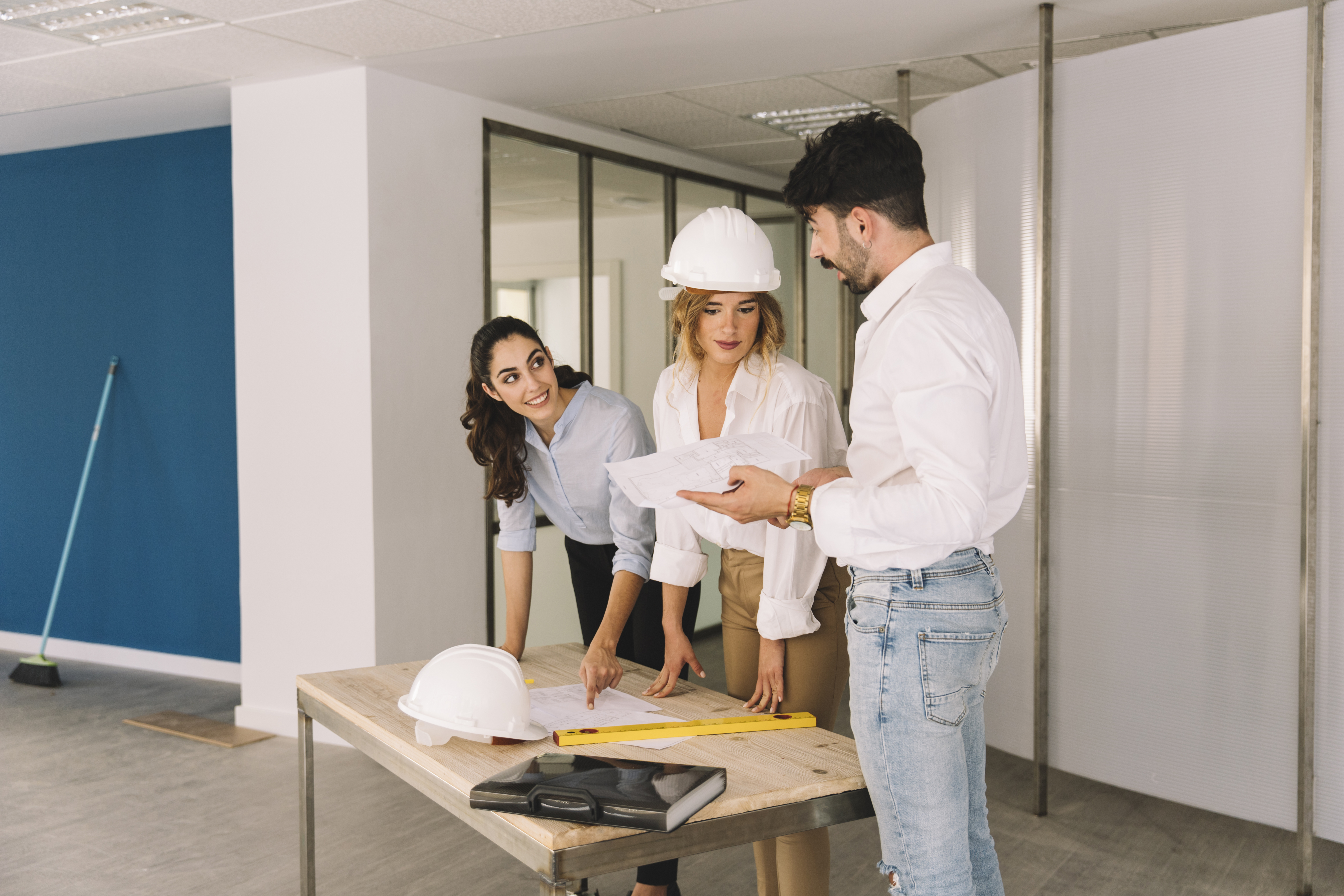 Ejecutivos y obreros con cascos revisando planos y cerrando un acuerdo para la planificación y ejecución del diseño de oficinas modernas en un edificio 